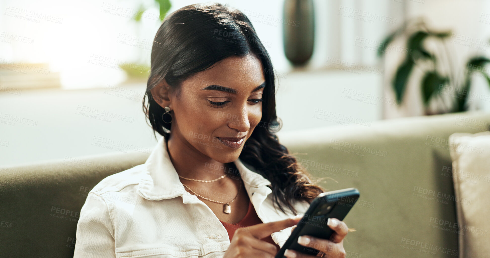 Buy stock photo Face, phone and search with Indian woman on sofa in living room of home for internet browsing. App, smile and social media with happy person in apartment for text message communication on weekend