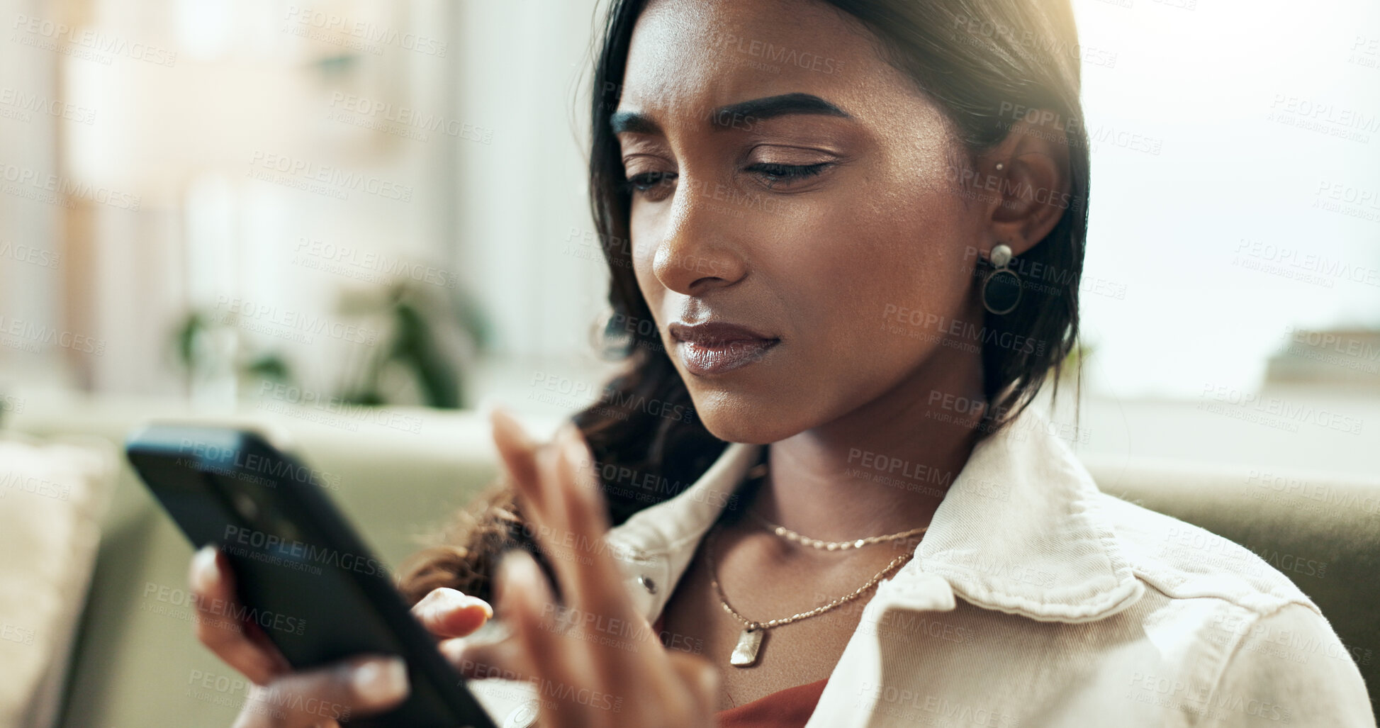 Buy stock photo Confused, phone and thinking with Indian woman on sofa in living room of home for online research. App, doubt and social media with annoyed person in apartment for problem solving on weekend