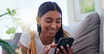 Girl, sofa and smartphone with scroll in home for social media browsing, reading ebook and smile for text message. Indian woman, person and happy with phone on couch for relax or comment on blog post