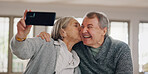 Senior couple, selfie and kiss in home, photography and online for social media post in living room. Elderly people, happy and laugh for affection in relationship, love and profile picture for memory