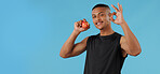 Man portrait, apple and okay sign for nutrition in studio, athlete and fruit for diet on blue background. Male person, like emoji and and approval for healthy snack, mockup space and promote fiber