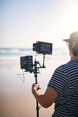 Buy stock photo Videographer, man and video camera at ocean for film, photography production and nature documentary. Cameraman, recording and shooting with equipment outdoor for filmmaking at beach, holiday and back