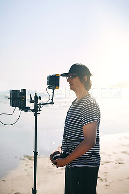 Buy stock photo Videographer, man and camera at beach for video, photography production and nature documentary. Cameraman, recording and shooting with equipment outdoor for filmmaking at sea, holiday film and mockup