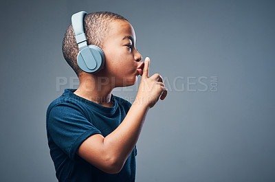 Buy stock photo Black kid, finger and lips for secret in studio with headphones for announcement, news and gossip. Boy, listening and music with privacy sign, confidential story and silence noise on gray background