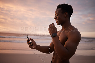 Buy stock photo Phone, earphones and black man at beach with fitness, smile and streaming music at sunset. Ocean, evening and happy runner with smartphone for video call, workout schedule or podcast on mobile app.