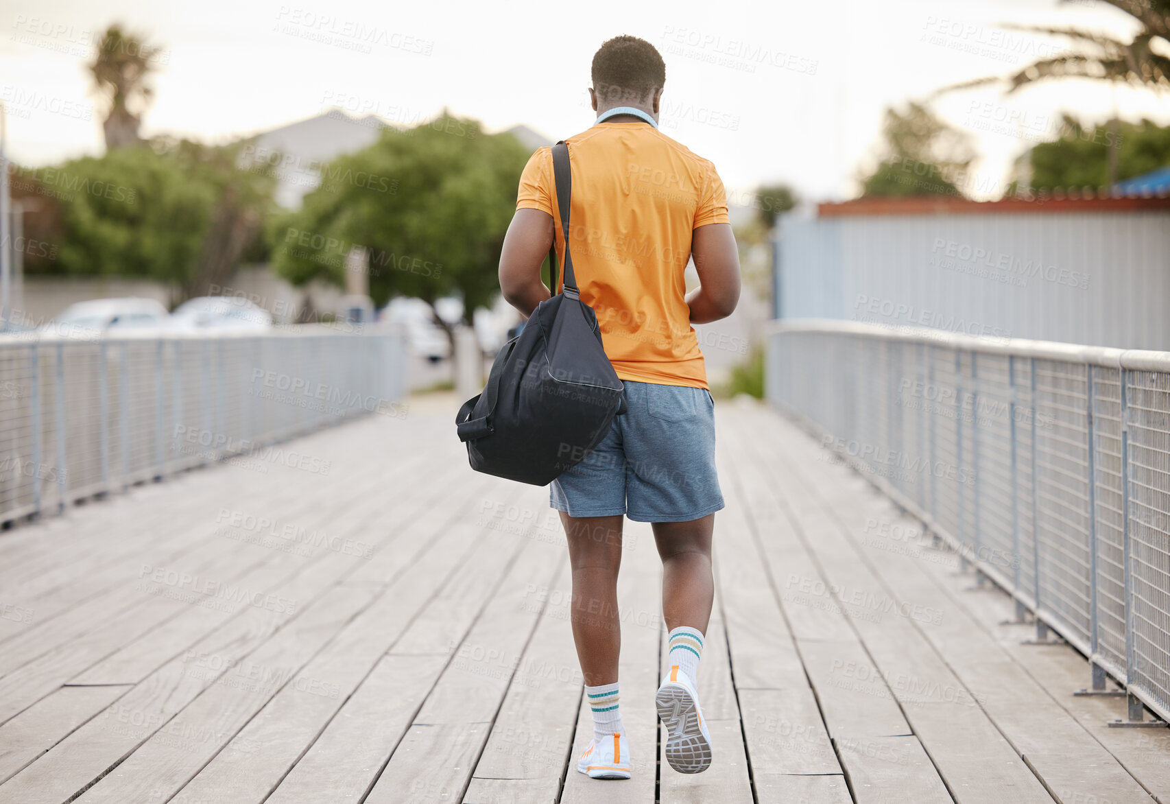 Buy stock photo Walking, fitness and back of man in city for exercise, training and warm up for workout outdoors. Runner, sports and African person with bag in urban town for health, wellness and running on bridge