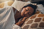 A beautiful young mixed race woman sleeping in a soft comfortable bed at home. One hispanic female feeling exhausted and resting in a comforting bed