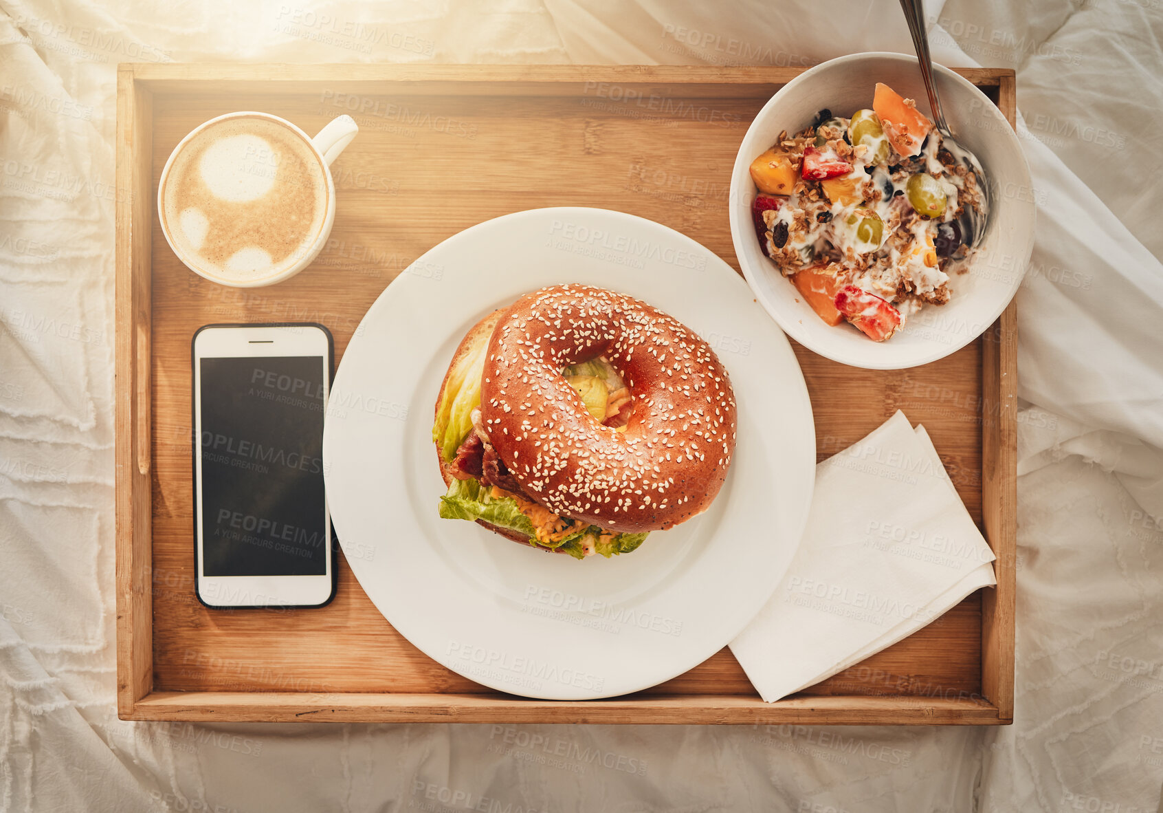 Buy stock photo Bagel, tray and food with coffee above on bed for room service, meal or breakfast at hotel. Top view, bread and snack with phone screen, cappuccino or muesli for catering or hospitality in bedroom