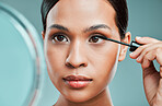 An attractive young woman using an spoolie brush and a mirror to comb her eyebrows against a green studio background. Hispanic female grooming her face by applying stylish makeup