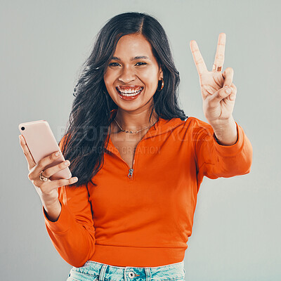 Buy stock photo Portrait, woman and phone with peace sign in studio for comic fun, communication and creative opinion. Smile, girl and mobile with v emoji for trendy clothes, stylist aesthetic and gray background