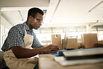 Focused businessman typing an email. Young fashion designer working on his laptop. Creative entrepreneur working in his design workshop. African American tailor ordering stock online with his computer