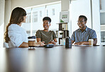 Three young happy businesspeople having a meeting while sitting at a table at work. Cheerful business professionals talking and planning in an office together