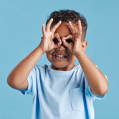 Buy stock photo Boy, hands and binoculars sign for studio portrait with smile for search, vision and zoom by blue background. Child, fingers and eyes with ok emoji for perspective, playful and icon in Costa Rica