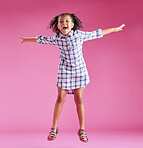 A pretty little mixed race girl with curly hair celebrating and dancing against a pink copyspace background in a studio. African child jumping and feeling free