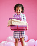 A pretty little mixed race girl with curly hair holding a stack of wrapped presents against a pink copyspace background in a studio. African child looking excited about getting gifts for her birthday