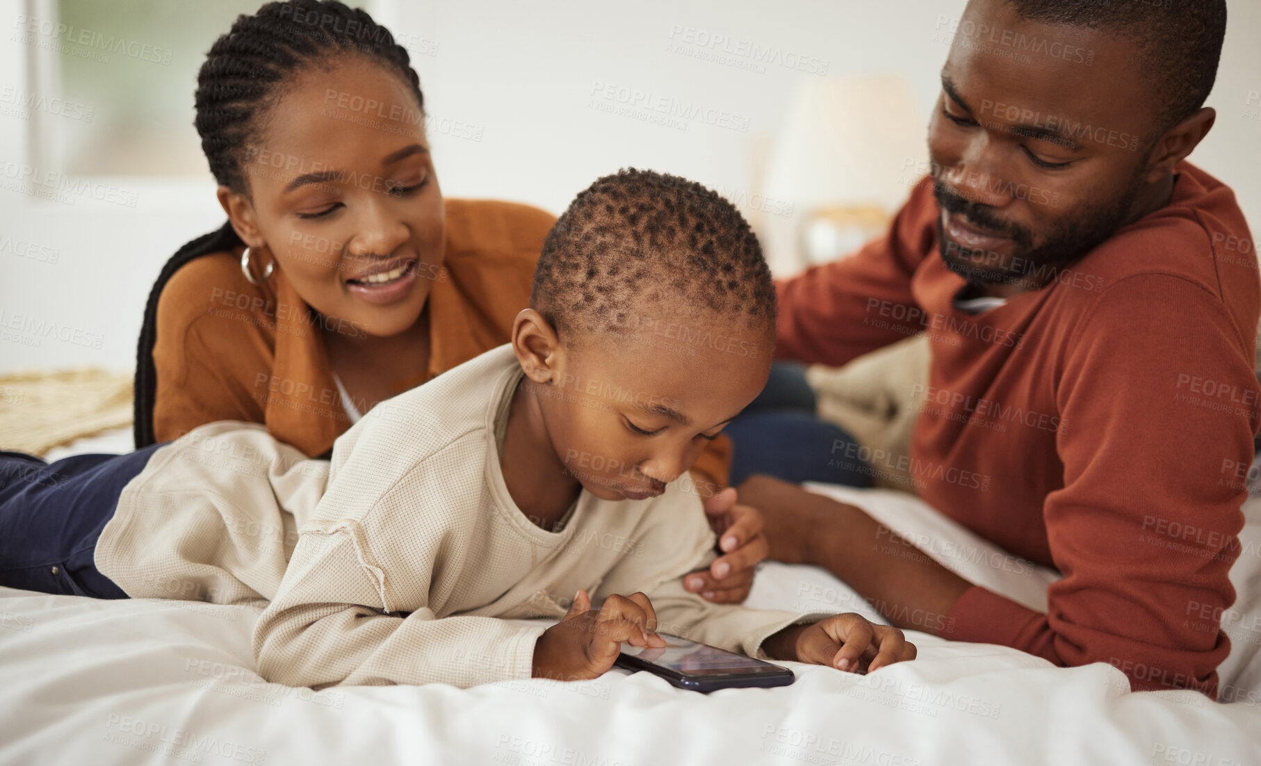 Buy stock photo Happy, phone and African parents with child on bed for bonding, relax together and relationship in home. Family, love and mom, dad and boy on smartphone in bedroom for playing, online videos and fun