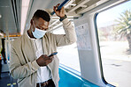 Black businessman travelling alone. A young african american businessman using a cellphone while standing in the passage on a train during his commute to the city