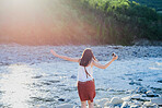 Carefree woman hiking over river to take photos of nature on her digital camera.Woman on holiday alone crossing a river over rocks holding her digital camera. Woman crossing river with digital camera