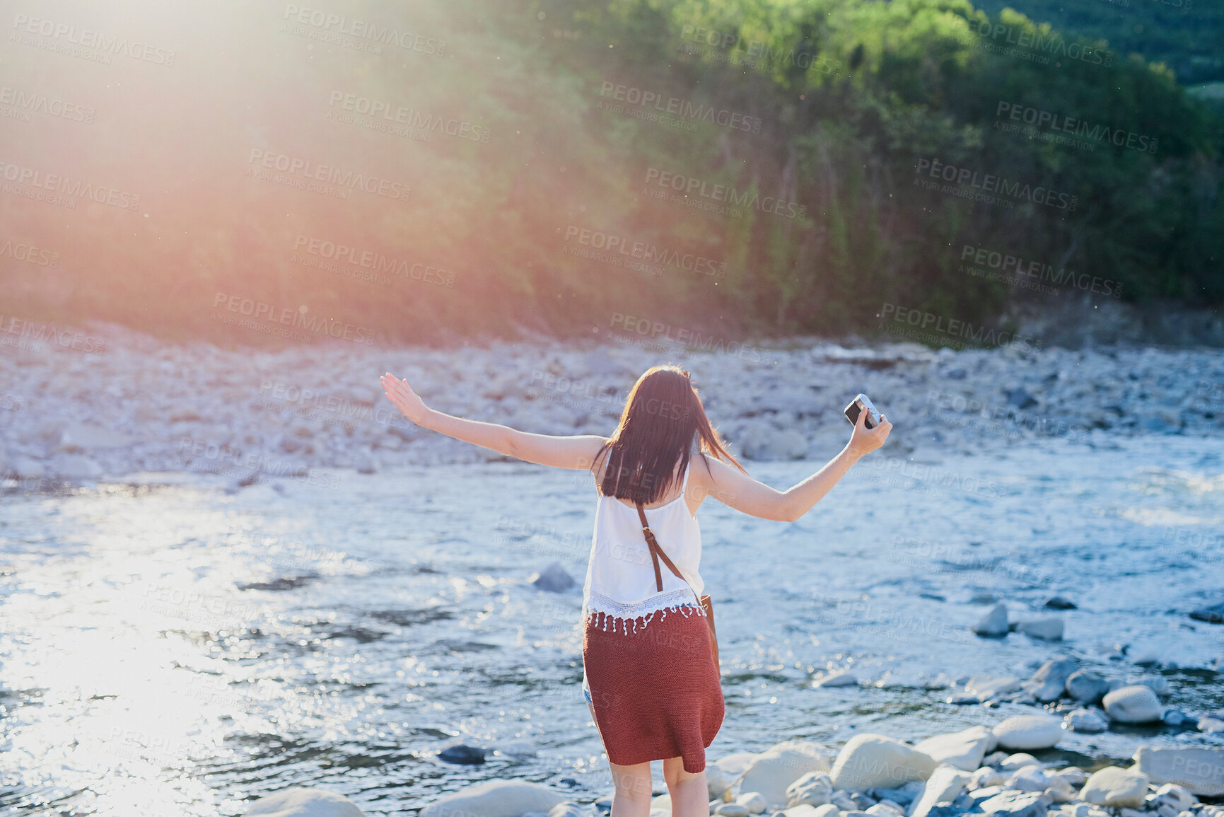 Buy stock photo Back, woman and camera in river for travel, journey and summer adventure in nature. Girl, digital tech and balance at water for crossing, wilderness vacation or freedom in environment for photography