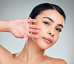 Portrait of a beautiful mixed race woman touching smooth soft skin in a studio. Hispanic model with healthy natural glowing skin looking confident against grey copyspace while doing routine skincare