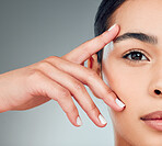 Portrait of a beautiful mixed race woman with smooth soft skin in a studio. Hispanic model with healthy natural glowing skin looking confident against grey copyspace while doing routine skincare