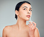 A beautiful young mixed race woman with glowing skin posing against grey copyspace background. Hispanic woman applying lipstick in a studio