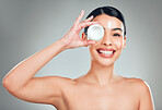 Studio Portrait of a beautiful smiling mixed race woman applying cream to her face. Hispanic model with glowing skin holding moisturiser against a grey copyspace background