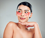 A beautiful mixed race woman wearing under eye patches. Hispanic model with glowing skin using hydrating treatment against a grey copyspace background