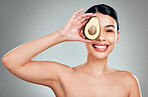 Studio Portrait of a beautiful young mixed race woman holding a sliced avocado. Hispanic model with glowing skin holding a fruit against a grey copyspace background