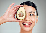 A happy mixed race woman holding an avocado. Hispanic model smiling and promoting the skin benefits of a healthy diet against a grey copyspace background