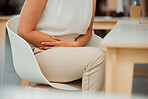 Closeup of one mixed race business woman holding sore tummy while feeling ill with menstrual stomach cramps and belly ache in an office. Hungry employee on period getting sick, bloated and uncomfortable with digestive pain caused by stress and anxiety