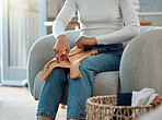 Woman sitting on a chair folding laundry. Woman cleaning her clothing, doing housework. Woman doing chores at home. Mixed race woman completing cleaning duties. Woman folding a basket of clothing