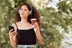 One young mixed race woman enjoying the city and using her cellphone to listen to music through headphones while drinking a takeaway coffee. Hispanic woman browsing the internet on a phone downtown