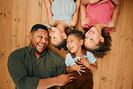 A happy mixed race family of four relaxing and lying on the lounge floor together. Loving black single parent bonding with his kids while being affectionate at home