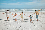 Rear view of a playful mixed race family with three children running on the beach with arms outstretched. A big family spending time and enjoying holiday by the sea