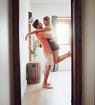 Happy young boyfriend holding girlfriend in arms as he lifts her up while they look into each others eyes and share intimate moment. Romantic young couple hugging and enjoying passionate dance at home