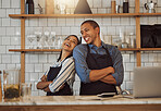 Cheerful businesspeople standing in their cafe kitchen. Business partners standing back to back in their coffeeshop. Two entrepreneurs arms crossed in their restaurant kitchen.