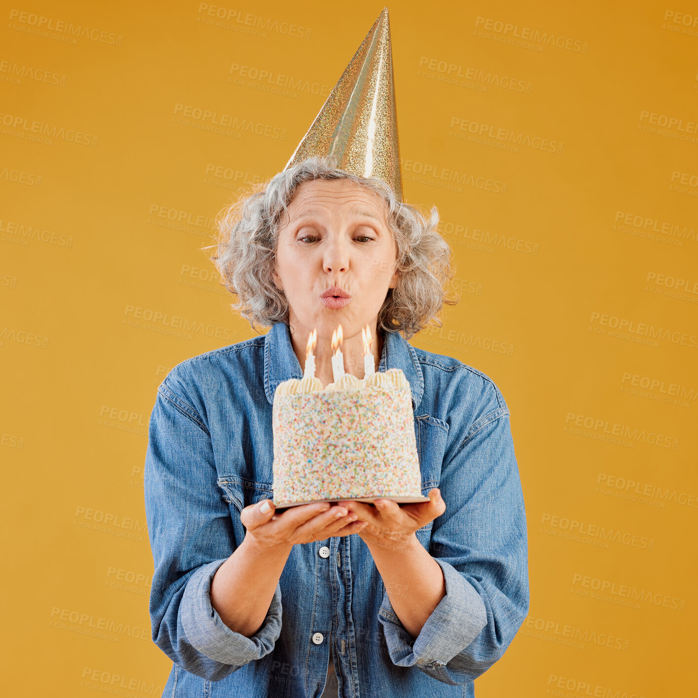 Buy stock photo Studio, mature woman and birthday cake with candles for blow flame, wish and celebration party. Female person, present and event gift with hat for sweet candy dessert, milestone and yellow background