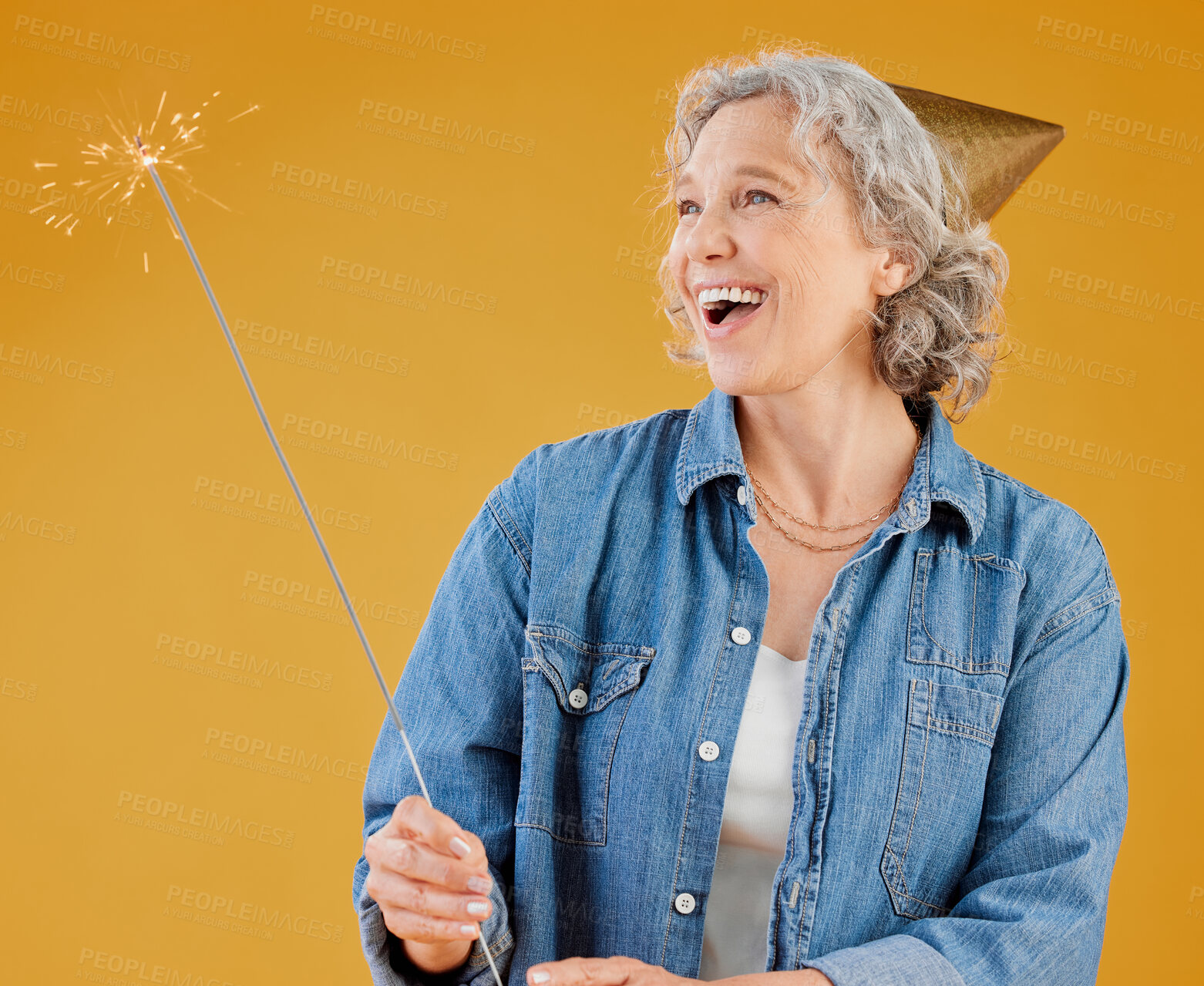 Buy stock photo Birthday, party hat and sparkler with mature woman in studio isolated on yellow background for celebration. Fireworks, milestone and retirement with happy senior person in casual outfit for carnival