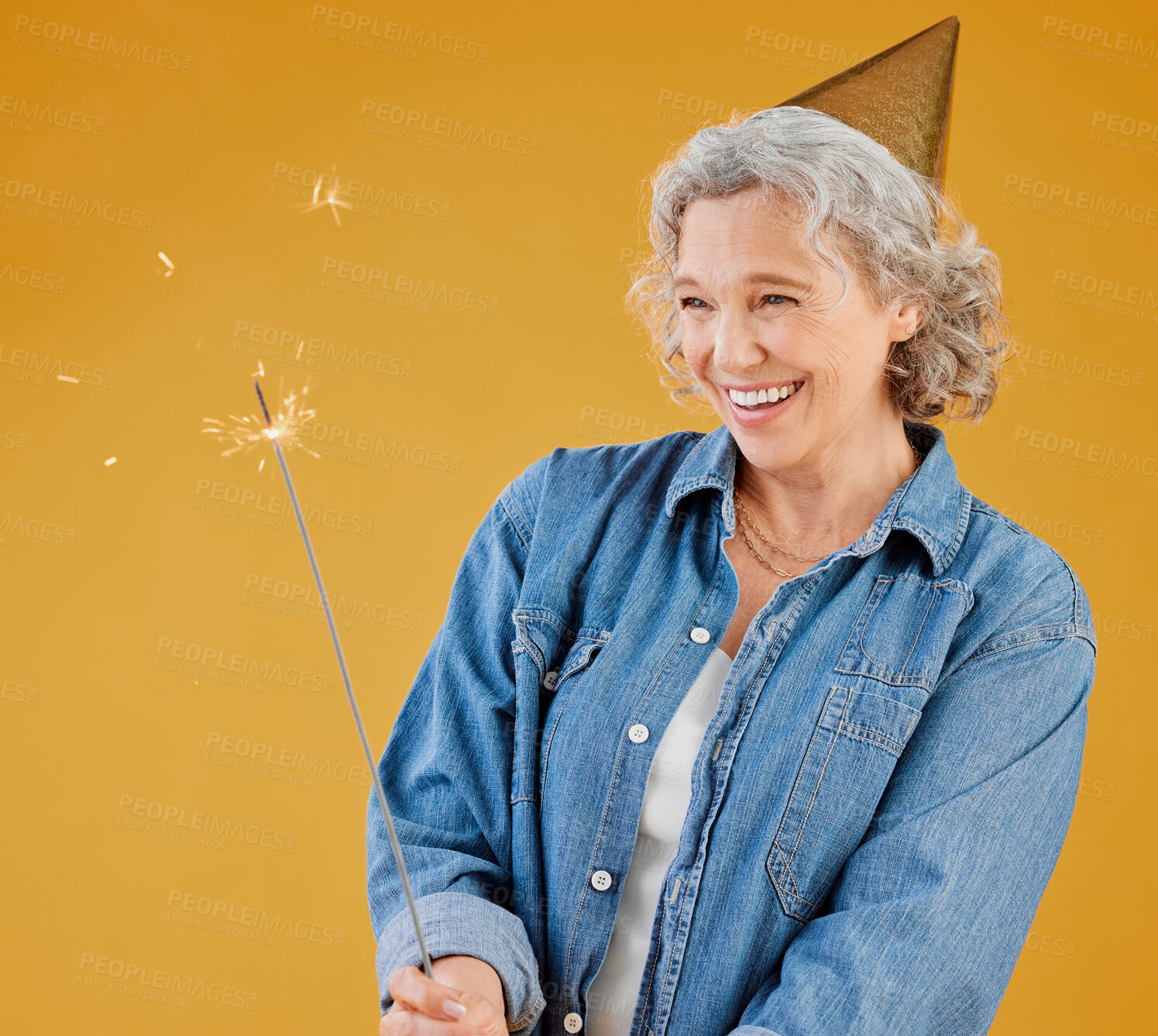 Buy stock photo Birthday hat, party and sparkler with mature woman in studio isolated on yellow background for celebration. Event, fireworks and and retirement with happy senior person in casual outfit for carnival