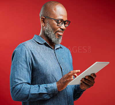 Buy stock photo Mature, black man and typing with tablet in studio for research or social media on a red background. African, male person or model with smile on technology for online browsing, app or news on space