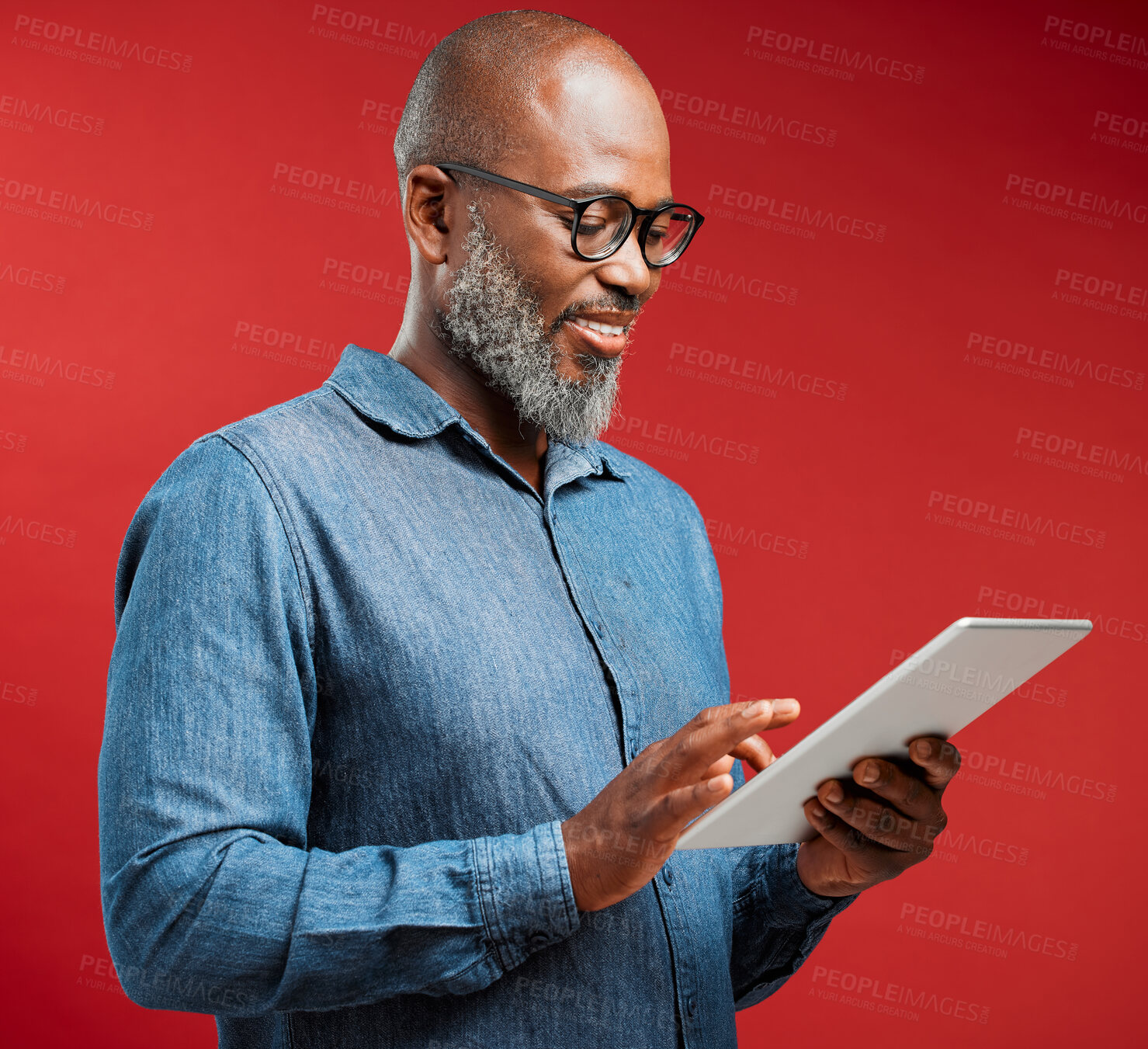 Buy stock photo Mature, black man and typing with tablet in studio for research or social media on a red background. African, male person or model with smile on technology for online browsing, app or news on space