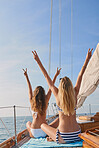 Excited young women with their arms raised cheering making peace signs on cruise. Happy friends on holiday making peace signs sitting on a boat. Women cheerfully making peace signs during a cruise