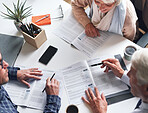 A mature couple meeting with a financial advisor to discuss retirement plans from above. A senior couple meeting a banker to sign contracts together. A mature couple reading and signing documents