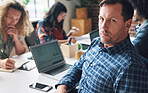 Portrait of a mature serious businessman sitting at his desk in his office with a group of diverse coworkers. A serious, leading businessman in his office with his staff.