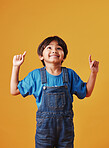 Adorable little boy looking cheerful wearing casual clothes and pointing his finger up against an orange copyspace  background. Little boy with an idea while having fun