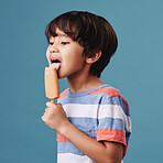 One adorable little asian boy looking happy while enjoying a sweet treat against a blue background. Mixed race child eating a sugar popsicle in summer