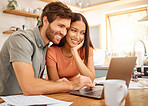 Young cheerful interracial couple bonding while typing on a laptop together at home. Caucasian boyfriend and girlfriend working through their bills and using a laptop. Cheerful husband and wife browsing online on a computer