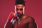 Portrait of one fit and strong handsome mixed race kickboxer isolated against a red studio background and getting ready to fight. Hispanic man posing shirtless in a punching stance. Focused on target