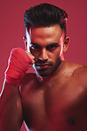 Portrait of one fit and strong handsome mixed race kickboxer isolated against a red studio background and getting ready to fight. Hispanic man posing shirtless in a punching stance. Focused on target